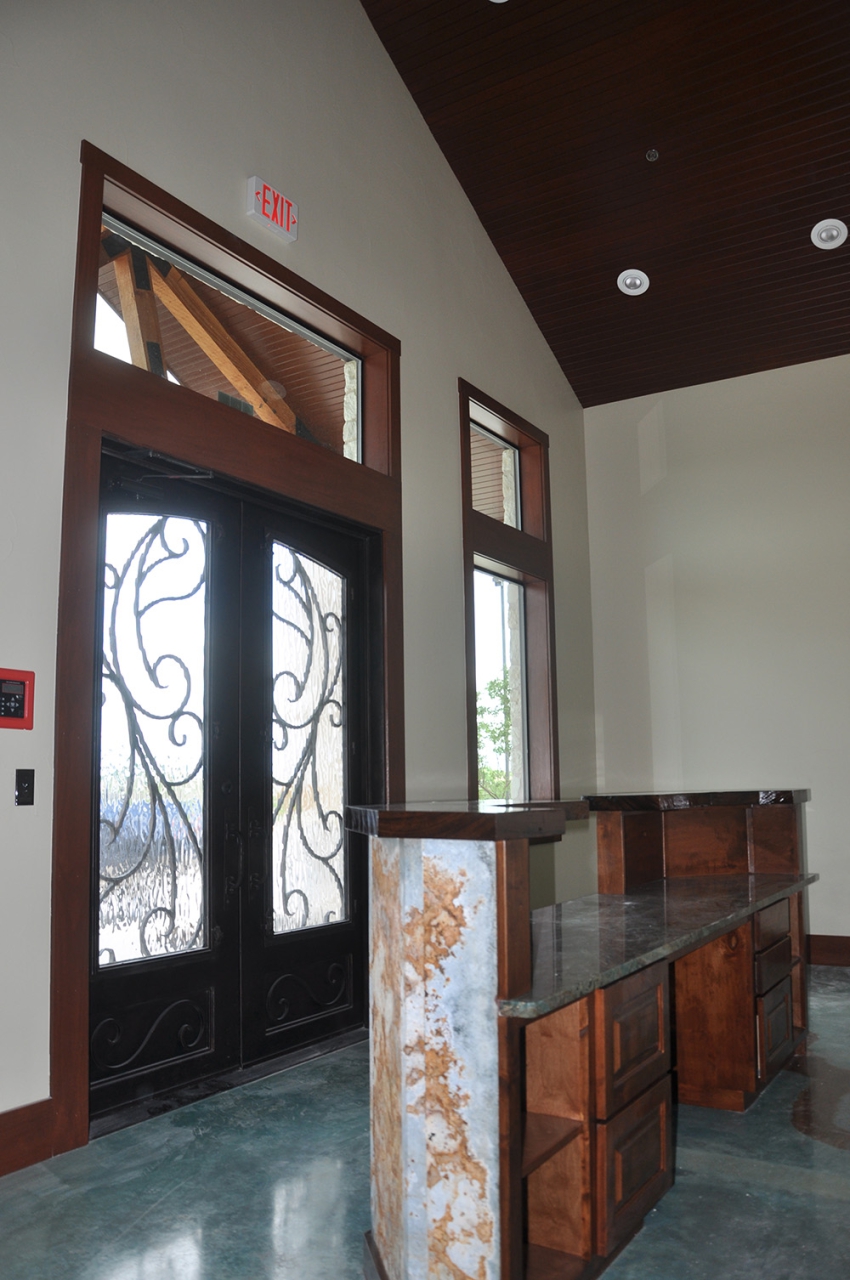 Construction Consulting and contracting in Central Texas. Ornate wood, glass, and iron front door from the inside, showing marble, granite, and dark wood receptionist desk and blue apoxy flooring.