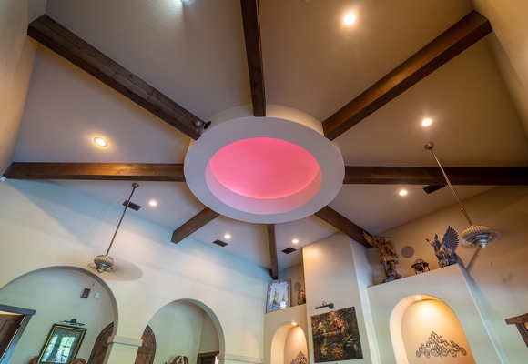 Custom inset light in center of luxury living room. Tall ceilings and wood beams. Imported art on shelves and walls.