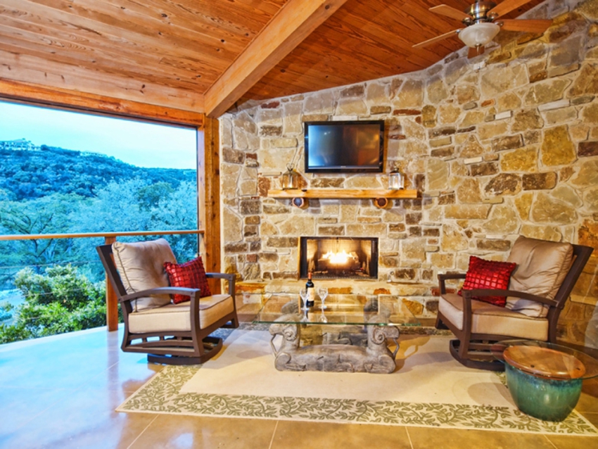 Covered patio with fireplace overlooking the Texas hill country outside of Wimberley. TV mounted on a stone wall. Custom built home by SB Thompson Construction and Contractors.