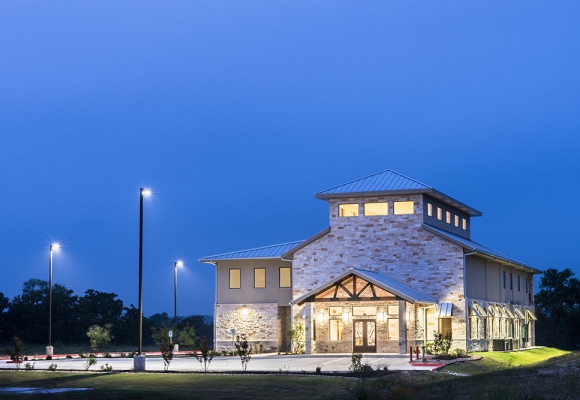 Construction Consulting and contracting in Central Texas. 2 story building with Limestone front and oak beams. Ornate wood, glass, and iron front door. large parking lot. Photo taken at night.