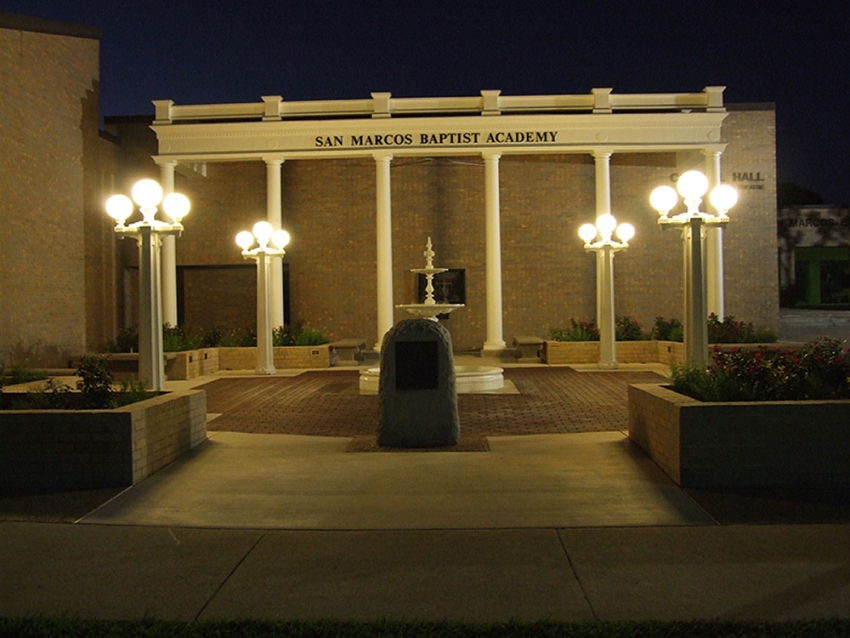 Remembrance gardens at night built for San Marcos Academy by contractors managed by SB Thomspson construction. Stone and concrete pathways, tall white columns, a decorative white fountain, white lighting and rose garden.