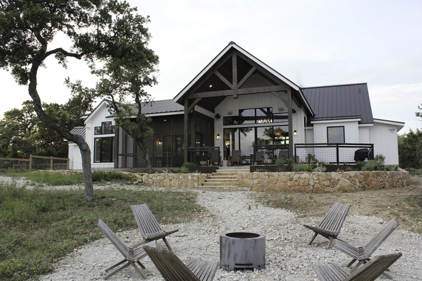 Custom Home black and white built by SB Thompson in Wimberley, Texas. Small minimally landscaped back yard and patio, rock wall, and fire pit area